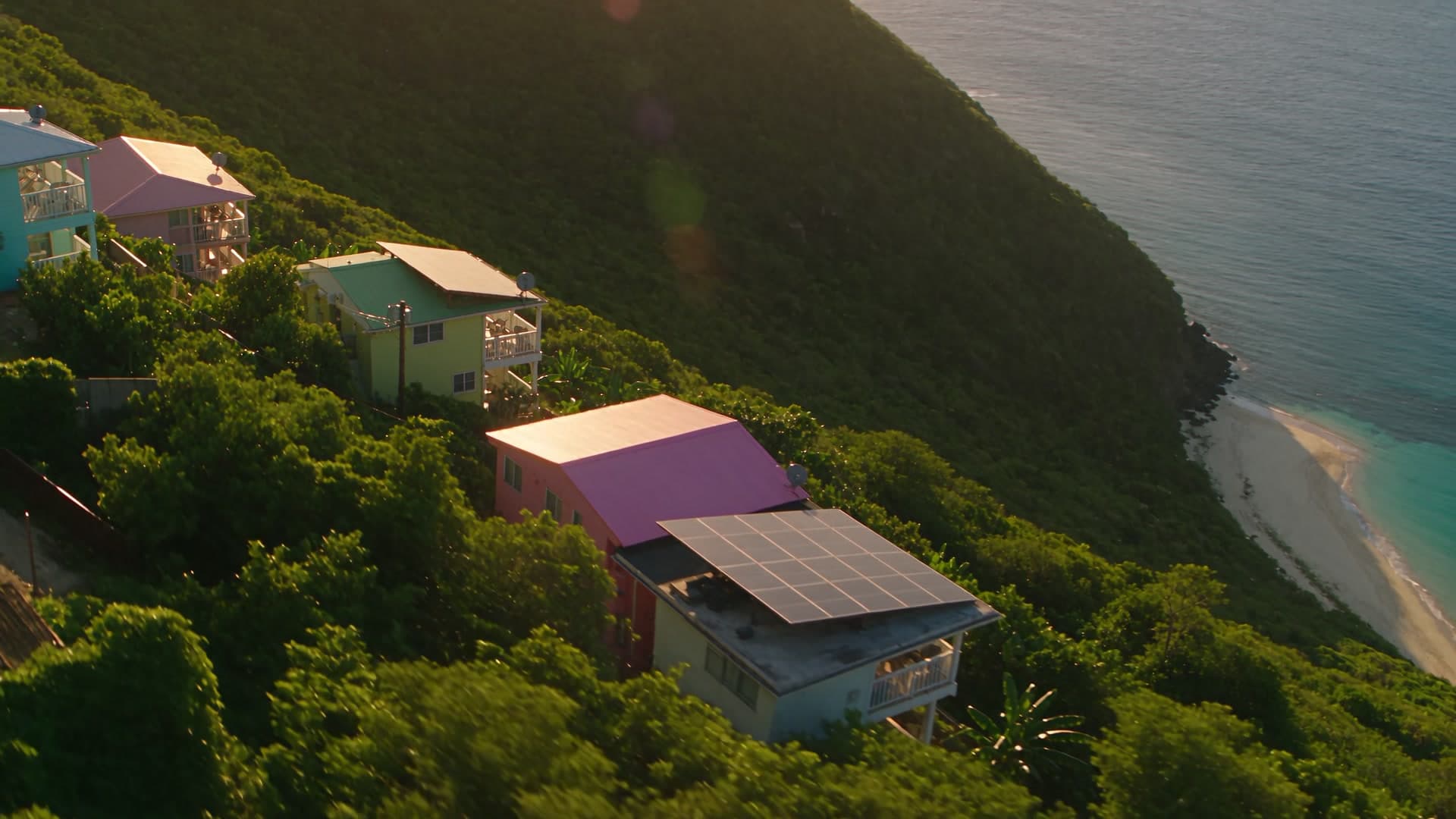 A Virgin Islands ridge of homes at golden hour, one carrying a rooftop solar array